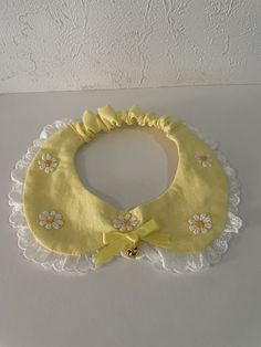 a yellow bib with white lace and flowers on the bottom, attached to a wall