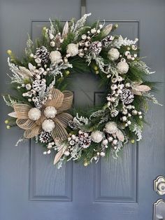 a christmas wreath hanging on the front door with white and silver decorations, pine cones, berries and mists