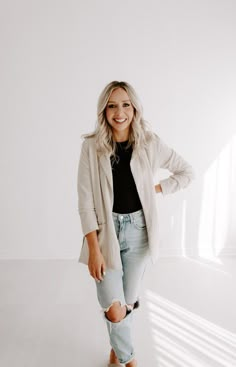 a woman standing in front of a white wall wearing ripped jeans and a blazer