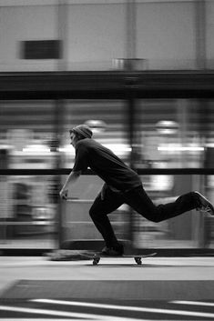 a man riding a skateboard down a street next to a tall building with lots of windows