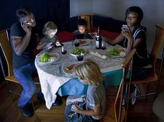 four people sitting at a table with food and wine in front of them, all looking at their cell phones