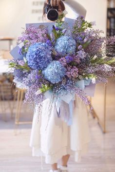 a woman holding a bouquet of blue and purple flowers in front of her face while taking a photo