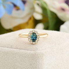 a blue diamond ring sitting on top of a white box with flowers in the background