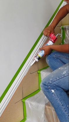 a woman is painting the wall with green tape and paint rollers while sitting on the floor