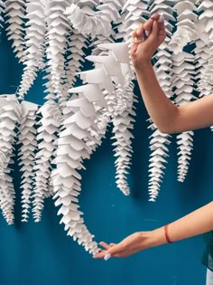 a woman standing in front of a blue wall with white paper hanging from it's sides