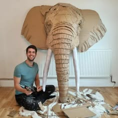 a man is sitting on the floor next to an elephant made out of toilet paper