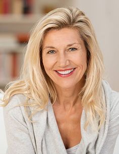 a woman with blonde hair smiling at the camera while sitting on a white couch in front of a bookcase