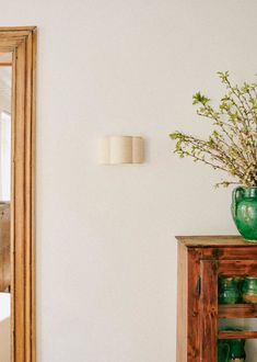 a green vase sitting on top of a wooden table next to a mirror and shelf