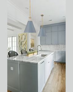 a large kitchen with blue cabinets and marble counter tops, two pendant lights hanging over the island