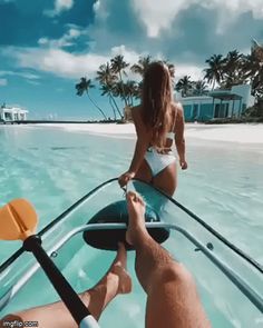 a man and woman riding on the back of a boat in clear blue water with palm trees