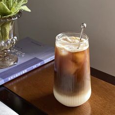 a drink sitting on top of a wooden table next to a vase filled with flowers