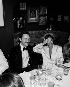 a group of people sitting around a table with wine glasses on it and one person covering his eyes