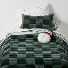 a bed with green and white checkered bedspread, pillows and a stuffed animal