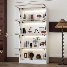 a white book shelf filled with books next to a lamp and pictures on the wall