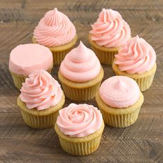 six cupcakes with pink frosting on a wooden table