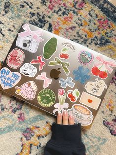 a person is holding an apple laptop with many stickers on the screen and it's cover