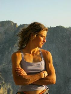 a woman with her arms crossed standing in front of a mountain