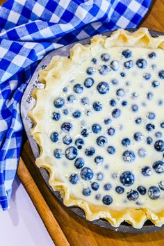 a pie crust with blueberries and cream in it on a cutting board next to a napkin