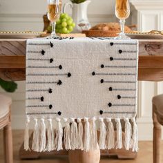 a table topped with a white and black table runner covered in tassels on top of a wooden table