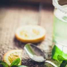 a glass filled with green liquid next to sliced lemons and mint leaves on a table