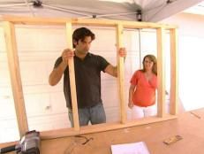 a man and woman standing in front of a mirror with framing on the wall behind them