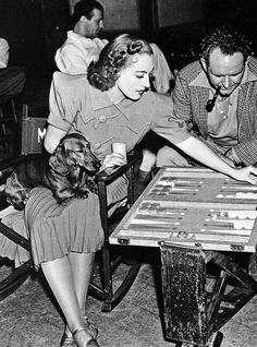 a man and woman playing checkers with a dog sitting at a table in front of them