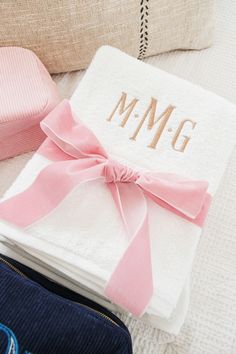 a personalized towel with a pink bow sits on a bed next to two pillows