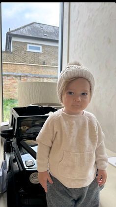 a little boy standing in front of an oven wearing a knitted sweater and hat