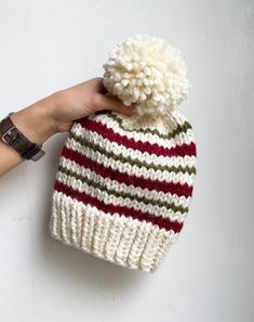 a hand is holding a knitted hat with a pom - pom