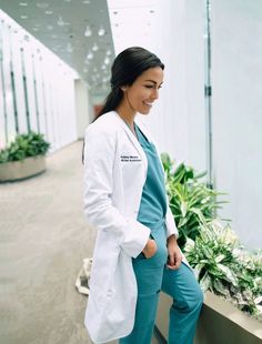 a woman in white lab coat and blue pants sitting on a ledge next to potted plants