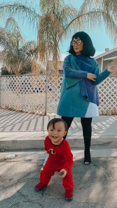 a woman standing next to a baby in front of a palm tree with her arms outstretched