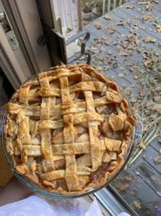 an apple pie sitting on top of a glass cake plate in front of a window