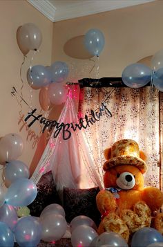 a large teddy bear sitting on top of a couch surrounded by balloons and streamers