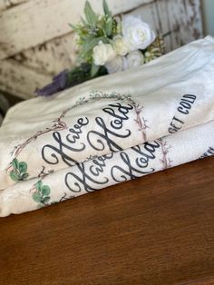 two white towels sitting on top of a wooden table next to a vase with flowers