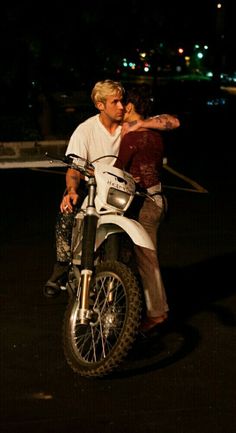 a man and woman riding on the back of a white motorcycle at night with their arms around each other