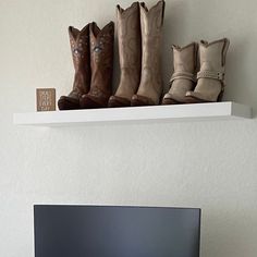 a flat screen tv sitting on top of a white shelf next to a pair of cowboy boots