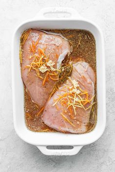 two raw pork chops in a white casserole dish with carrots and parmesan cheese