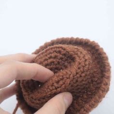 a hand holding a brown crocheted object in it's palm