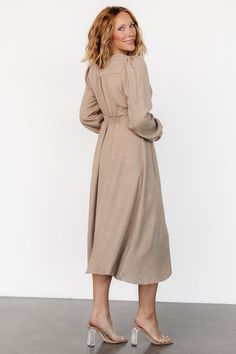 Casual and stylish all in one dress Lightweight linen-like material Neutral taupe color V-neckline Buttoned placard down front of dress Gathering at bust, shoulder yoke, and across back Long sleeves with single buttons at cuffs Upturned, paneled V-waistband with subtle gathering underneath Elastic at back waist Unlined 63% Recycled Polyester, 37% Polyester Marianne is 5'6, cup size 34D, size 6 and wearing size S Modest Beige V-neck Dress, Elegant Linen Button-up Dress, Fall Beige Midi Dress With Button Closure, Beige Button Closure Midi Dress For Fall, Beige Button-up Midi Dress, Spring Taupe V-neck Dress, Elegant Neutral Button-up Dress, Beige Button-up Linen Dress, Elegant Beige Linen V-neck Dress