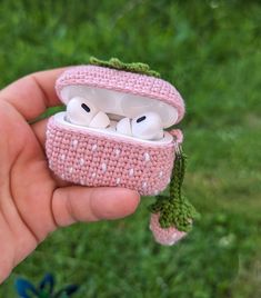 a hand holding a small pink case with two white ear buds in it's mouth