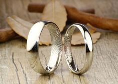 two wedding rings sitting next to each other on top of a wooden table with leaves