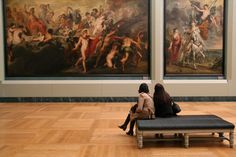 two women are sitting on a bench in front of some art work at the museum