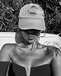 a woman wearing a hat with the word paris on it sitting in front of some bushes