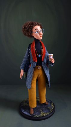 a doll with glasses holding a cup in her hand and standing on a black surface