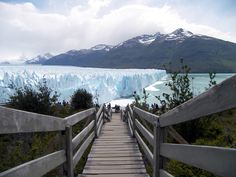 a wooden walkway leading to a glacier with mountains in the background and people walking on it