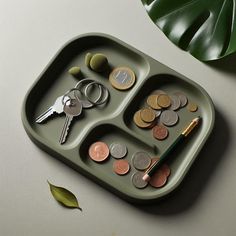 a tray filled with coins and keys on top of a table next to a plant