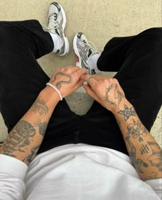 a man with tattoos on his arms and legs sitting down next to another person's feet