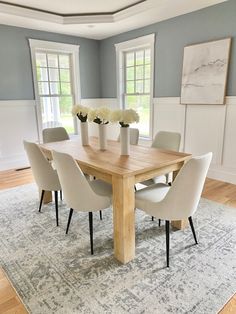 a dining room table surrounded by white chairs and vases with flowers in them on a rug