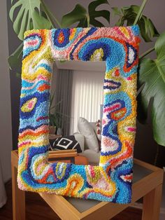 a multicolored frame sitting on top of a wooden table next to a potted plant