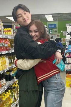 two people hugging each other in front of a grocery store aisle filled with drinks and condiments